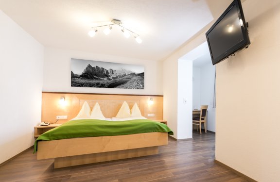 Helles Zimmer mit Doppelbett, TV und Bergfoto in Schwarz-Weiß