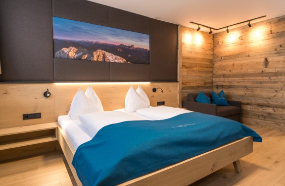 Modernes Doppelzimmer mit Holzdesign, Sofa und Bergbild über dem Bett