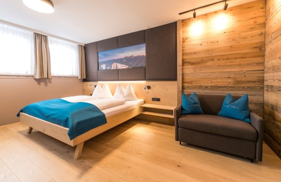Modernes Zimmer mit Doppelbett, Holzwand und gemütlichem Sofa