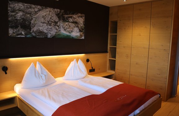 Modernes Schlafzimmer mit Doppelbett, weißen Kissen, roter Decke und Holzschrank rechts