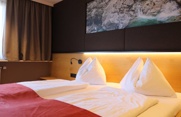 Gemachtes Doppelbett mit weißen Kissen, roter Decke und Landschaftsbild über dem Kopfteil