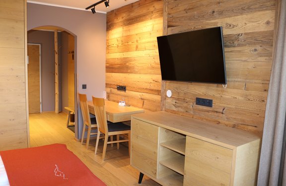 Holzvertäfelte Hotelzimmerwand mit Fernseher, Schreibtisch mit Stühlen und Kommode