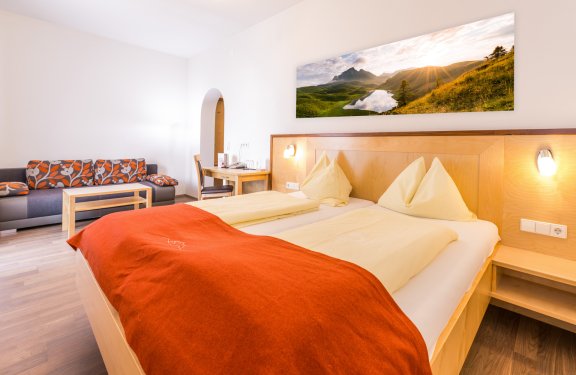 Helles Zimmer mit Doppelbett, rotem Plaid und gemütlicher Sitzecke mit Sofa