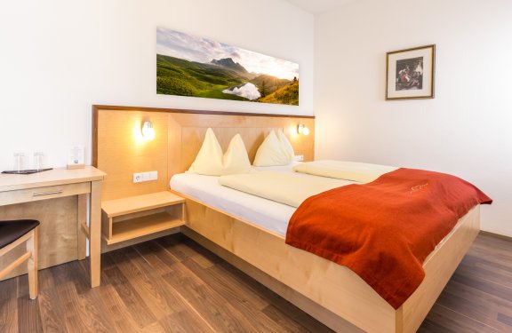 Zimmer mit Doppelbett, rotem Überwurf und Schreibtisch auf Holzfußboden