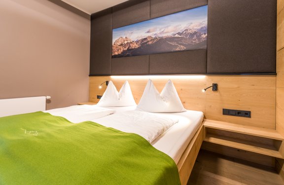 Modernes Schlafzimmer mit Doppelbett, grünem Überwurf und Bergbild über dem Kopfteil