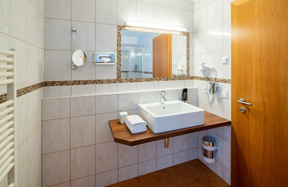 Helles Badezimmer mit rechteckigem Waschbecken auf Holzplatte, großem Spiegel und Holztür rechts
