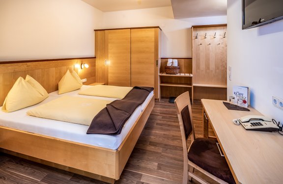 Hell eingerichtetes Hotelzimmer mit Doppelbett, Schrank, Schreibtisch und Garderobe