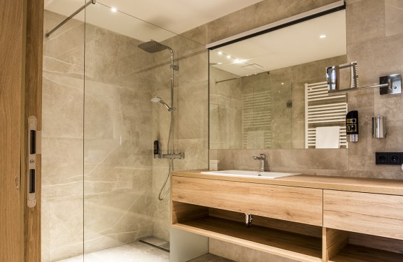 Helles Badezimmer mit begehbarer Dusche links und Holzwaschtisch mit Spiegel rechts