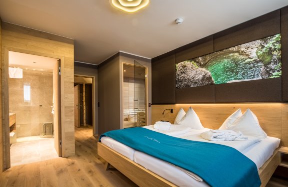 Modernes Hotelzimmer mit Doppelbett, blauer Decke, offenem Bad und Sauna mit Glastür
