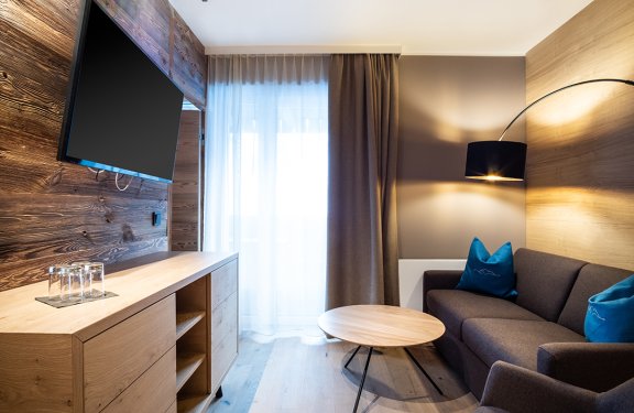 Modernes Wohnzimmer mit braunem Sofa, runden Holztisch, TV an Holzwand und Vorhängen vor Fenster