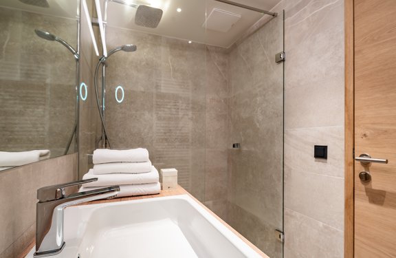 Moderner Badezimmerwaschbecken mit Handtüchern neben einer Glasdusche und Holztür
