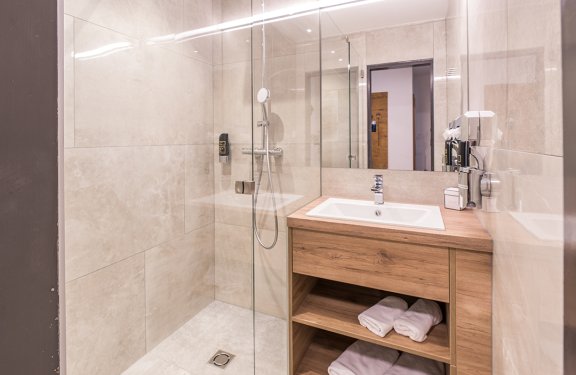 Helles Badezimmer mit Glasdusche links und Waschbecken auf Holzunterschrank rechts