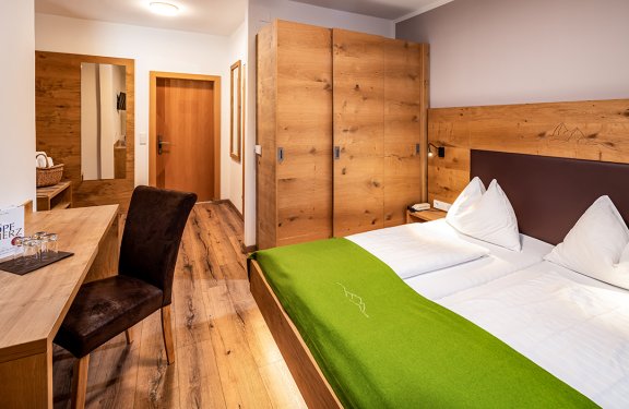 Schlafzimmer mit Holzmöbeln, grünem Bettüberwurf und Schreibtisch