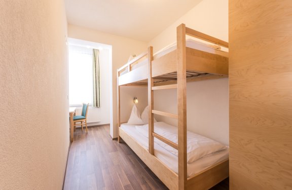 Stockbett in hellem, schmalem Raum mit Schreibtisch am Fenster