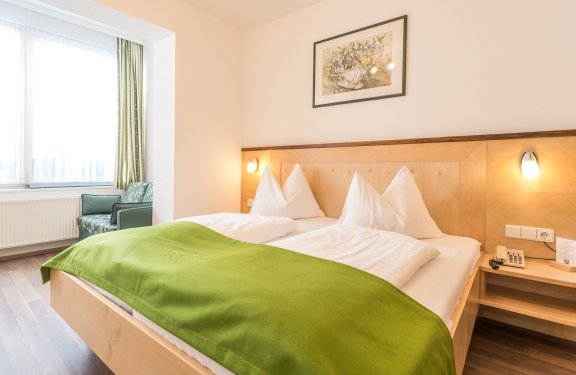 Doppelbett mit grüner Decke in hellem Zimmer mit Sessel am Fenster