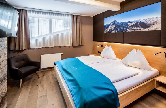 Doppelbett mit türkisfarbener Decke und Bergbild über dem Kopfteil