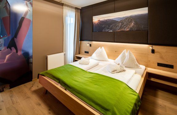 Doppelzimmer mit grünem Bettüberwurf und Bergfoto über dem Bett