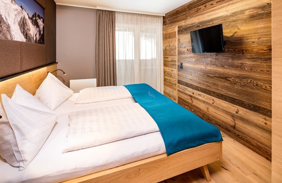Doppelzimmer mit Holzwandverkleidung und TV gegenüber dem Bett