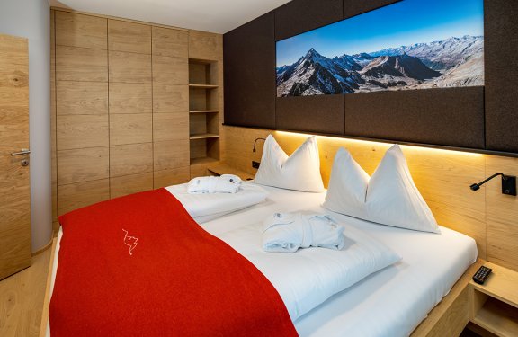 Doppelbett mit roter Decke und Panoramabild von Berglandschaft