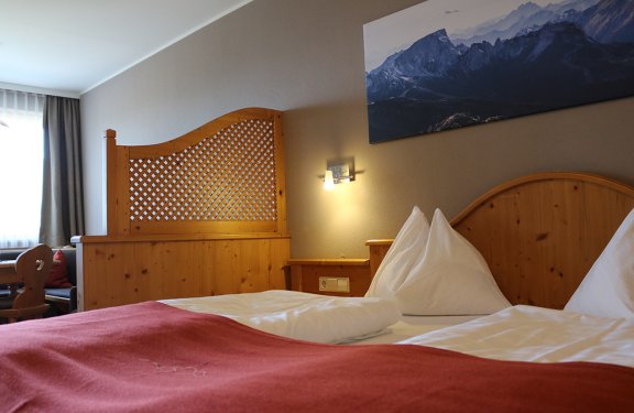 Gemütliches Hotelzimmer mit Holzmöbeln, roter Decke und Bergbild an der Wand