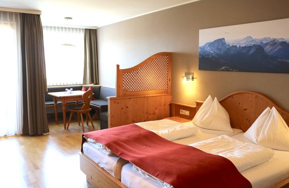 Hell eingerichtetes Hotelzimmer mit Doppelbett, Holzmöbeln und Sitzecke am Fenster