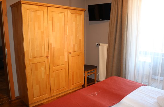 Holzkleiderschrank links neben einem Stuhl und einem Fenster mit Vorhängen im Schlafzimmer