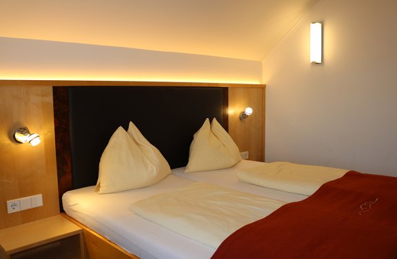 Gemütliches Doppelbett mit gelben Kissen und Decken, warmes Licht an der Wand