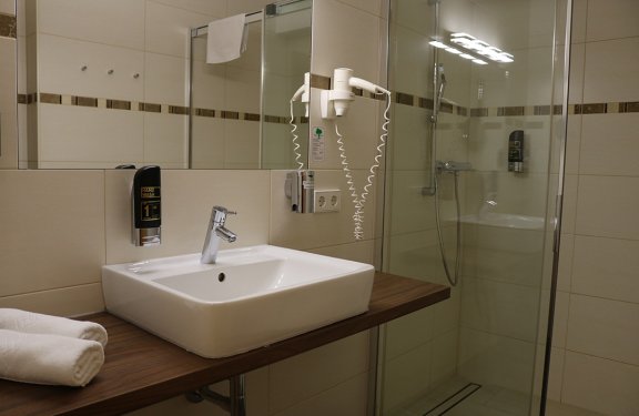 Moderner Badezimmerwaschbecken mit Handtüchern, Haartrockner und Duschkabine im Hintergrund