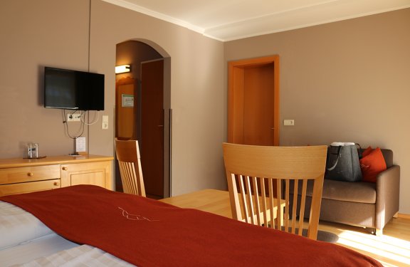 Blick auf ein Hotelzimmer mit Bett, Holzmöbeln, Fernseher und Sofa mit Tasche und Kissen