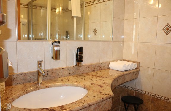 Badezimmer mit Marmorwaschbecken, Spiegel, Handwaschmittelspender und drei aufgerollten Handtüchern