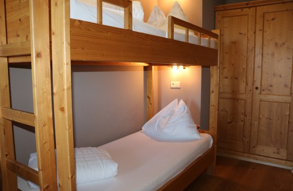 Holz-Etagenbett mit weißer Bettwäsche neben einem Holzschrank in einem Zimmer
