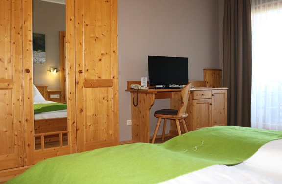 Hotelzimmer mit Holzmöbeln, grünem Bettüberwurf, Schreibtisch mit Fernseher und Stuhl