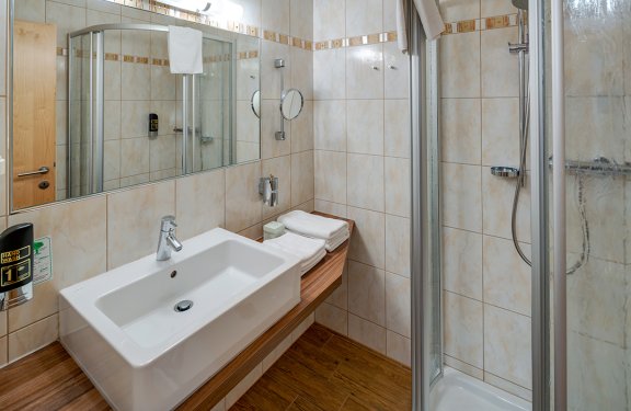 Kompaktes Badezimmer mit Waschbecken links, Spiegel und Dusche rechts mit Glastür
