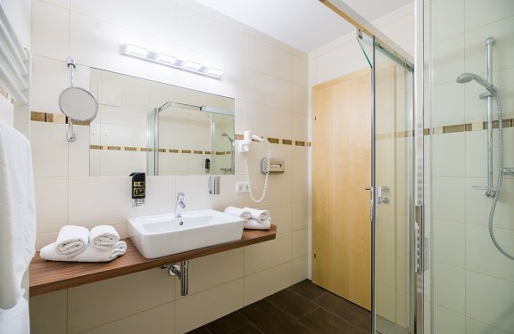 Helles Badezimmer mit Waschbecken auf Holzplatte, Handtüchern und Glastür zur Dusche rechts