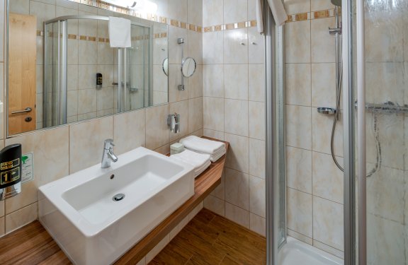 Badezimmer mit weißem Waschbecken, Dusche und großem Wandspiegel