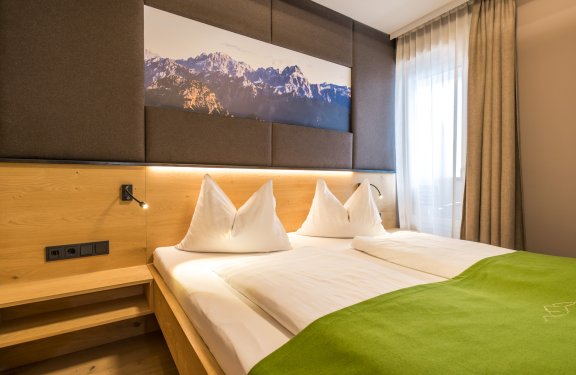 Modernes Doppelzimmer mit Holzelementen und Bergmotiv über dem Bett